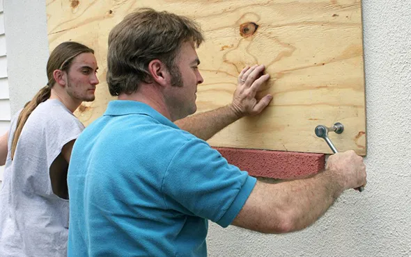Two people boarding up a window with wooden planks, showcasing local window board-up solutions in Desert Hot Springs, CA.