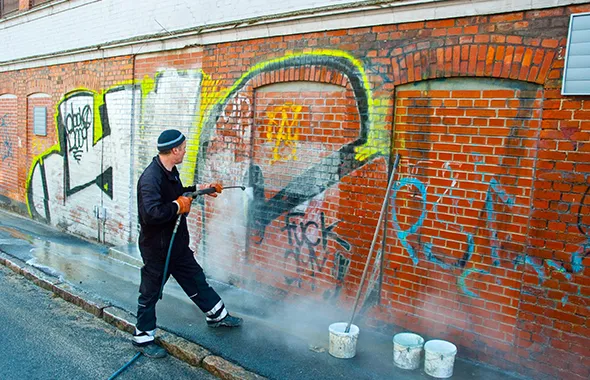 Professional assessing extensive graffiti covering a brick wall prior to trusted removal service in Desert Hot Springs.
